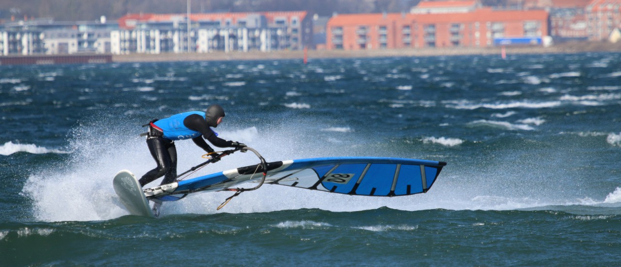 Windsurfer med blåt sejl i et sving på vandet